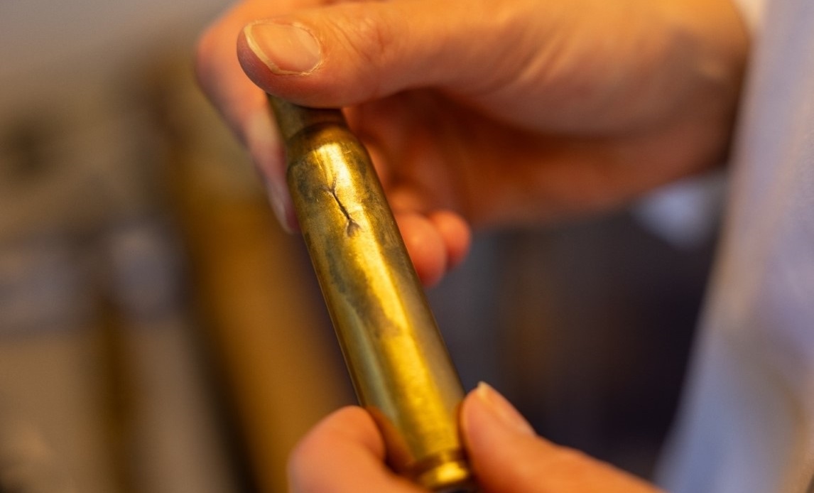 Revnen i patronhylstret er opstået lige på det punkt, hvor ammunitionsbæltet holder den fast.